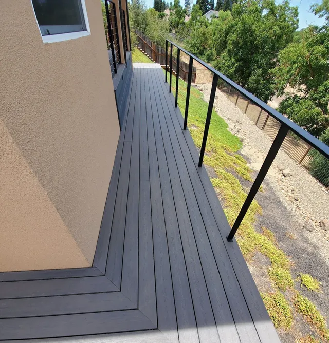 A modern dark gray composite deck wrapping around a tan stucco house exterior with a black metal railing.
