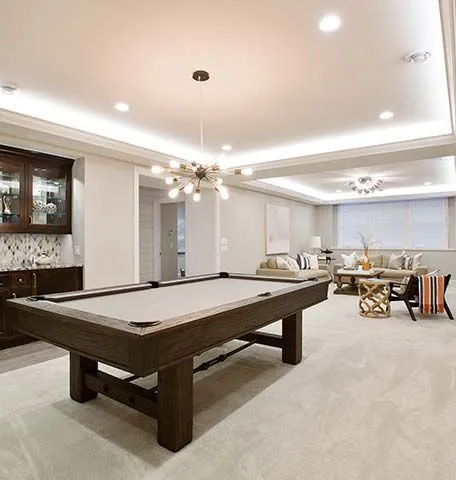 A basement game room featuring a wood pool table, recessed lighting, and a lounge area with seating and a wet bar.