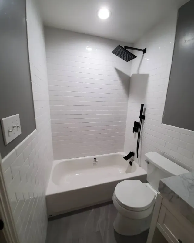 Small white bathroom with a bathtub, toilet, shower, and gray flooring. Small white bathroom with a bathtub, toilet, shower, and gray flooring.