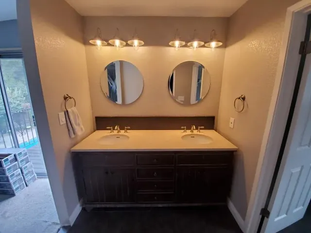 Modern bathroom vanity with double round mirrors, white countertop, and dark wood cabinets under wall sconces Modern bathroom vanity with double round mirrors, white countertop, and dark wood cabinets under wall sconces