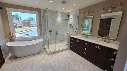 A luxurious bathroom with a white freestanding tub, glass shower, dark wood vanity, and large mirrors.