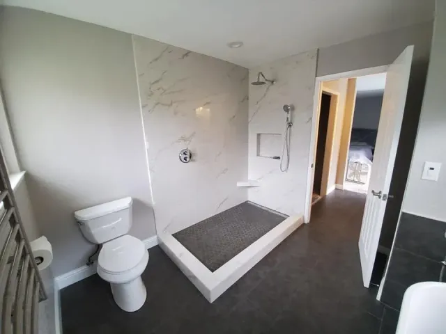 Modern bathroom with white toilet, tiled walk-in shower, and dark floor leading to an open doorway Modern bathroom with white toilet, tiled walk-in shower, and dark floor leading to an open doorway