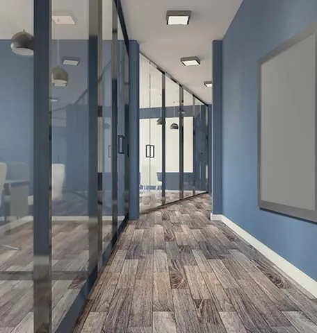 A perspective view of a modern office hallway with blue walls, wood-look flooring, glass partitions, and ceiling lights.