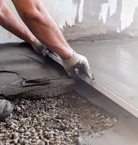 A worker wearing gloves uses a tool to level fresh concrete over a gravel base.