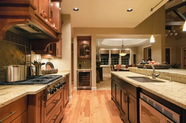 A luxury kitchen with wood cabinets, granite countertops, a gas range, a built-in wine cooler, and hardwood floors.