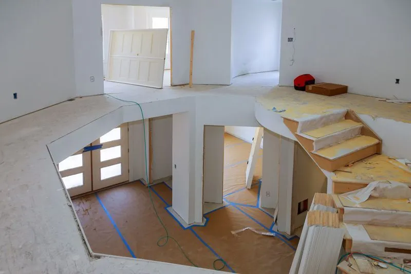An interior view of a two-story home under construction, showing a staircase, unfinished floors, and white walls.