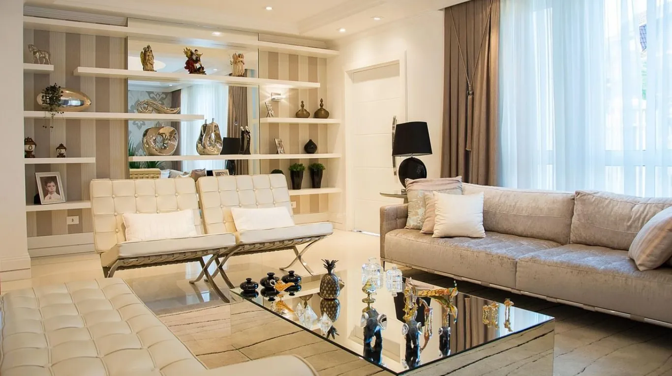 A brightly lit, modern living room with beige tufted sofas and a mirrored coffee table.