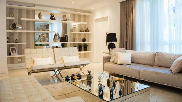 A brightly lit, modern living room with beige tufted sofas and a mirrored coffee table.