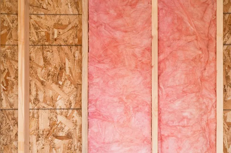 Wall studs framing an unfinished room, with pink fiberglass batt insulation installed between two vertical wooden beams.