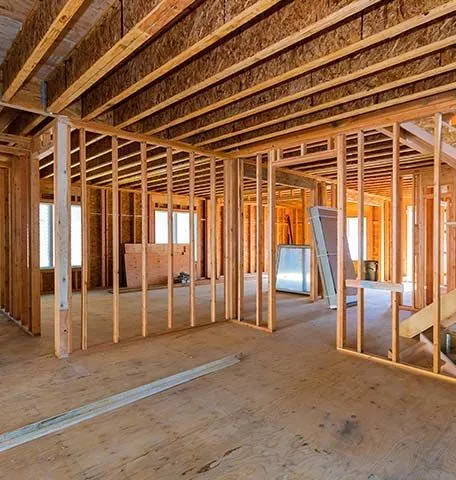 Interior view of a residential construction site featuring wooden wall framing and exposed floor joists.