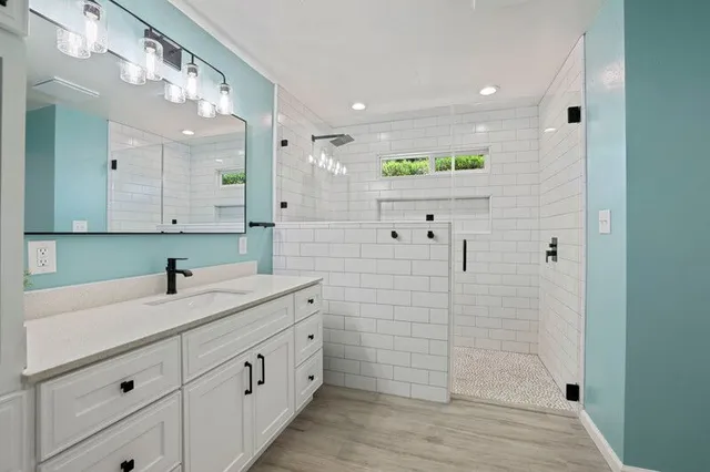 A modern bathroom with a white vanity, a large mirror, and a walk-in shower featuring white subway tiles and light blue walls.