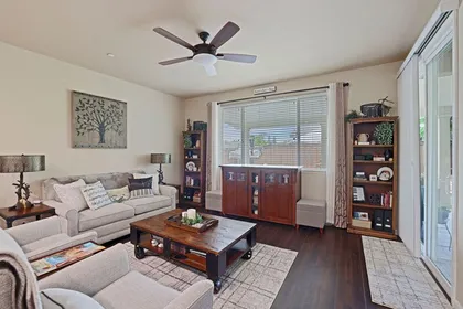 A living room with a beige sofa, two armchairs, a wooden coffee table, two bookcases, and a ceiling fan.