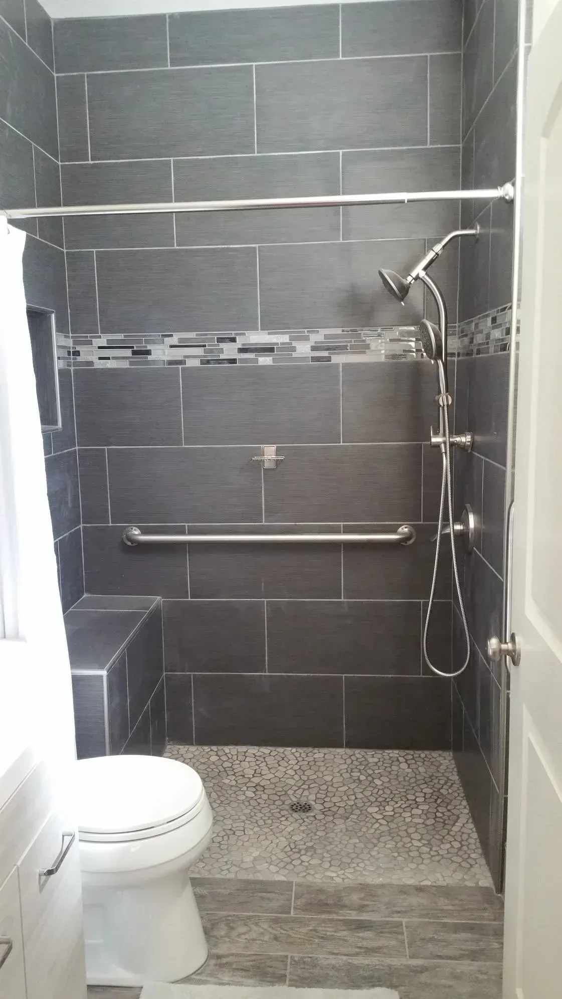 Small tiled bathroom with a toilet, shower, and gray wall tiles. Small tiled bathroom with a toilet, shower, and gray wall tiles.