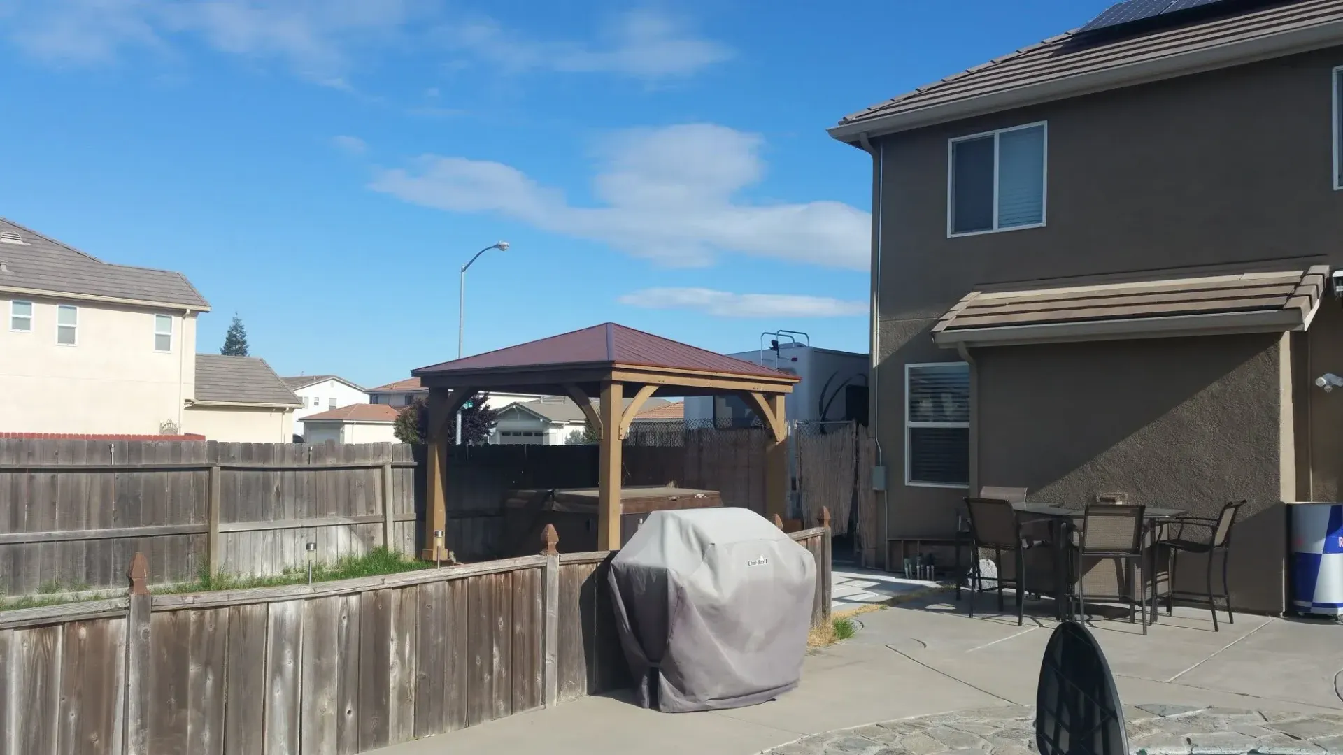 Backyard concrete patio with a covered gazebo, outdoor dining furniture, and barbecue grill in Galt