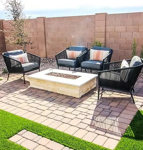 A modern patio seating area with four black woven chairs and a rectangular stone fire pit on a paver terrace.