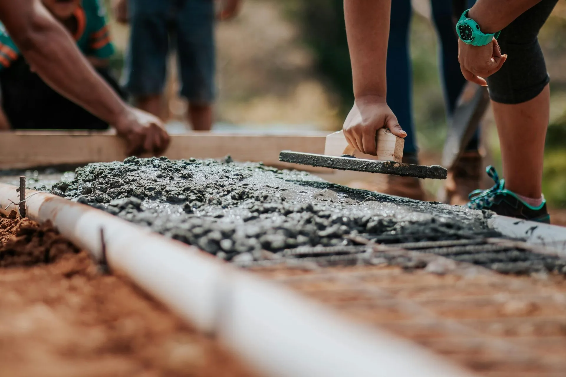A person uses a hand float to smooth wet concrete into a wooden form on a construction site.