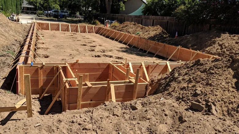 Wooden forms installed for a concrete foundation in an excavated construction site.