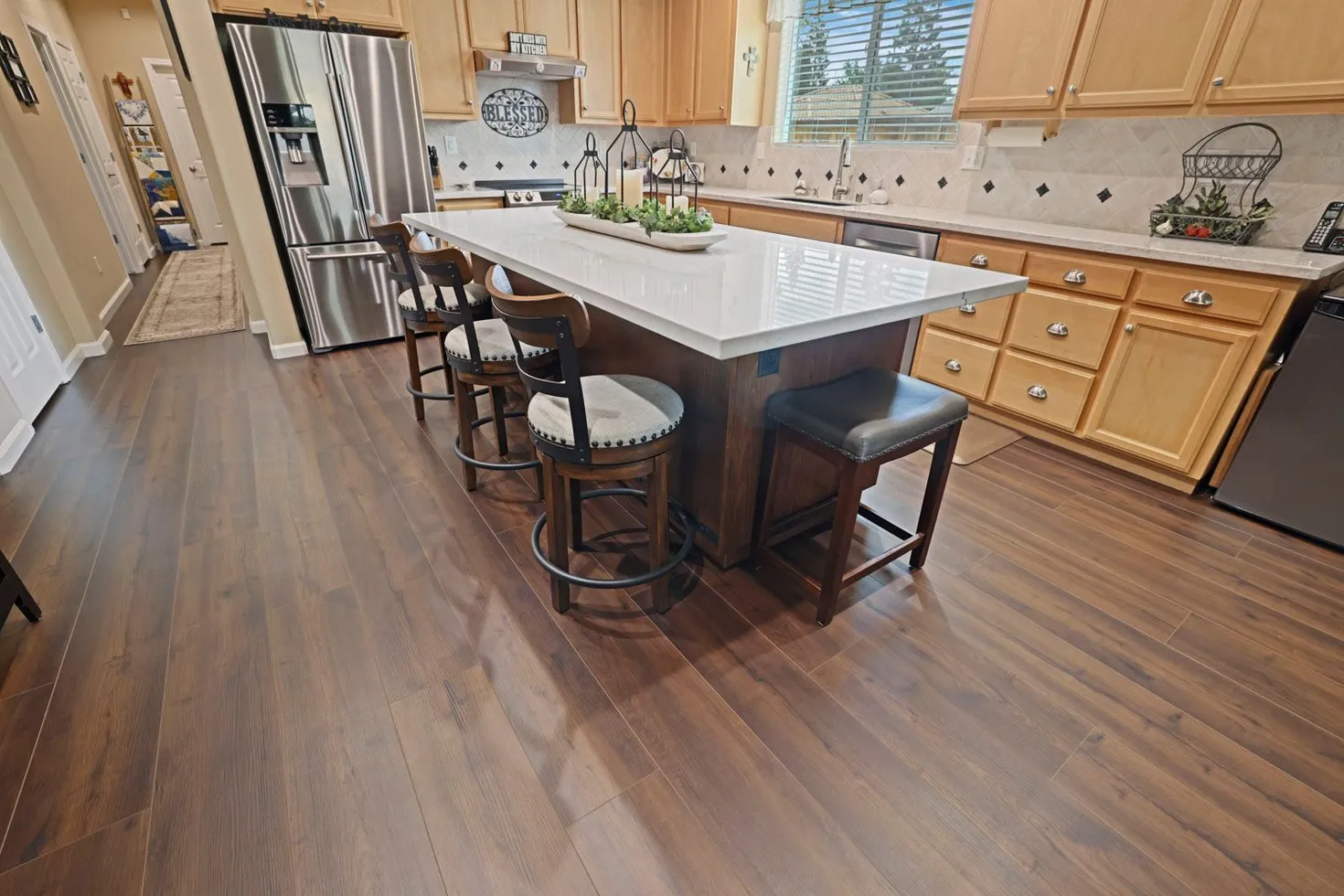 Kitchen featuring a center island with bar stools, stainless steel refrigerator, and wood cabinets on a dark floor.