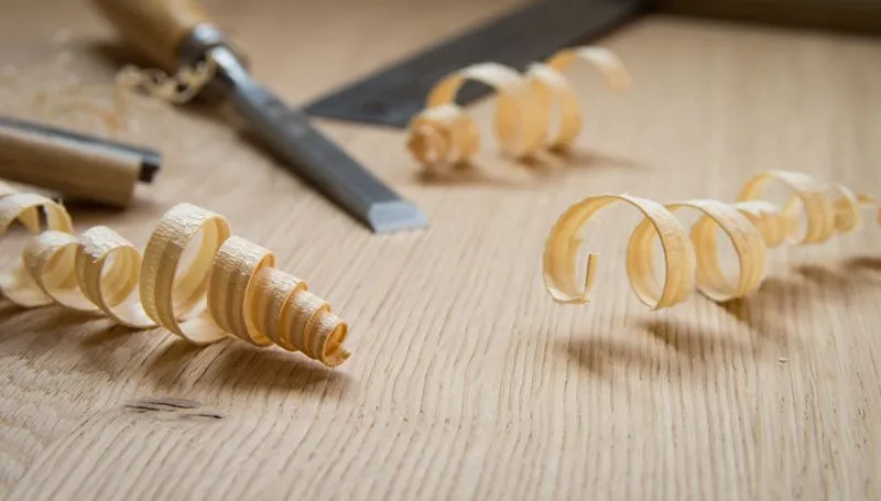 Wood shavings curled on a wooden surface next to a chisel and a square ruler.