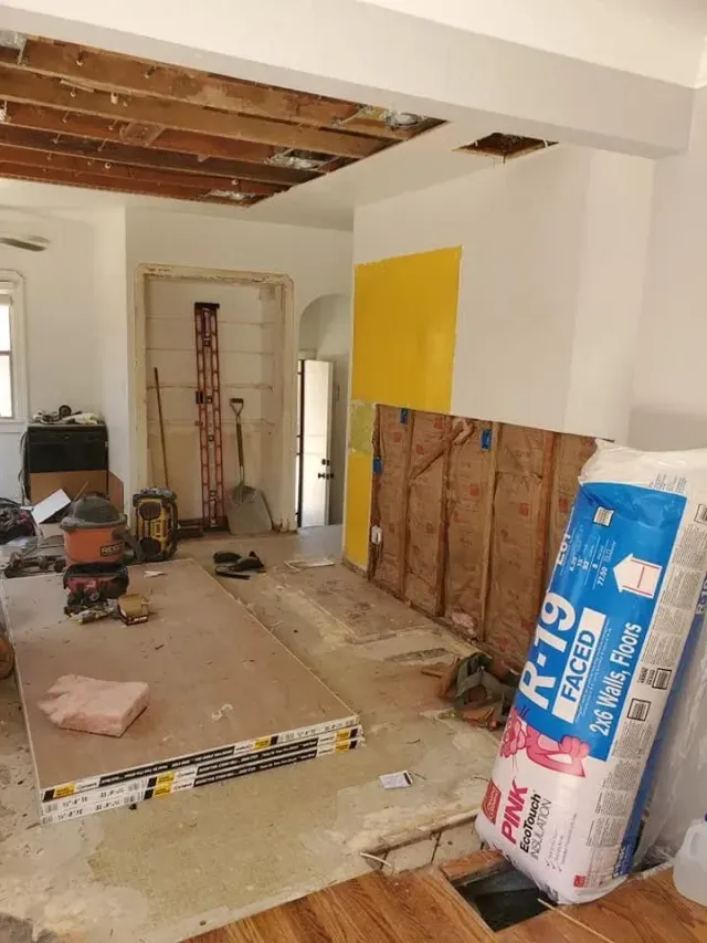 Renovation in progress in a room with exposed ceiling beams, tools, lumber, and a yellow wall patch