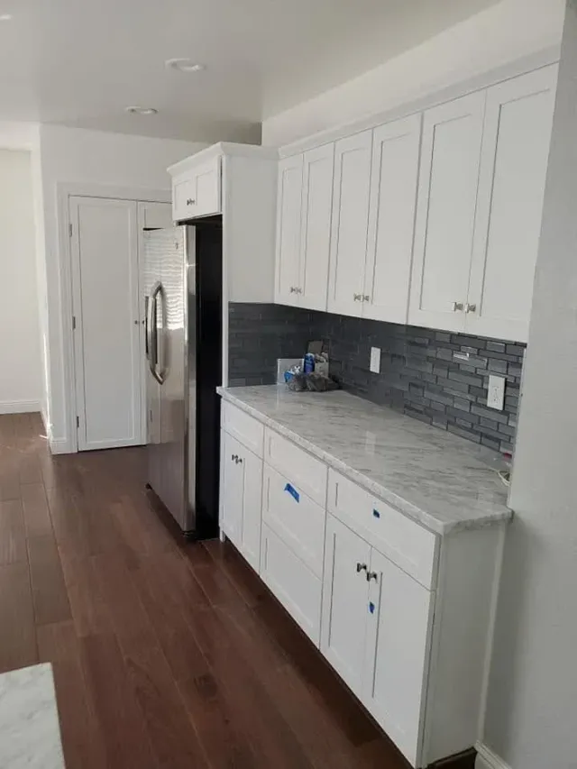 Modern white kitchen with stainless fridge, gray backsplash, and dark wood floors Modern white kitchen with stainless fridge, gray backsplash, and dark wood floors