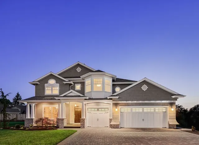 Two-story gray home with a stone-accented front porch and white garage doors at twilight.