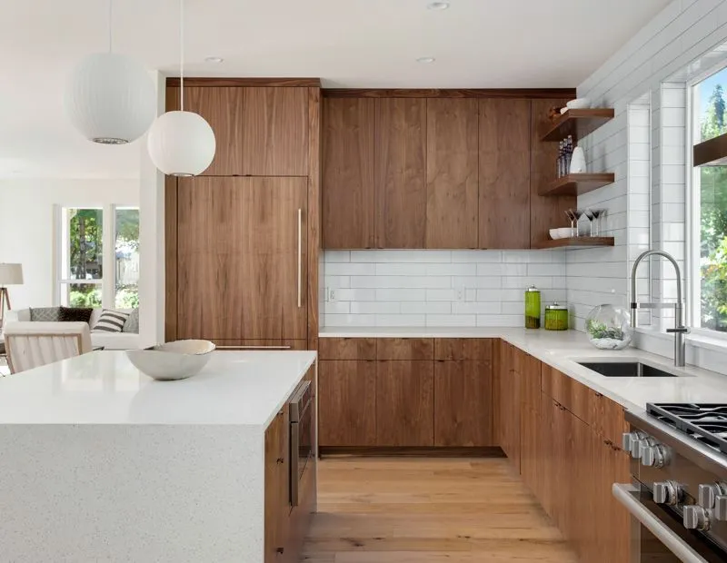 Modern kitchen with walnut cabinetry, white countertops, white subway tile backsplash, and two hanging globe lights.